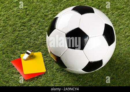 Soccer ball with referee yellow and red cards and chrome whistle on grass background - penalty, foul or sports concept, selective focus Stock Photo