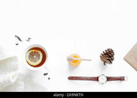 Winter cozy flat lay  -  Cup of Tea with lemon and honey, warm white sweater, pine cone and trendy watch isolated on white background. Minimal winter Stock Photo