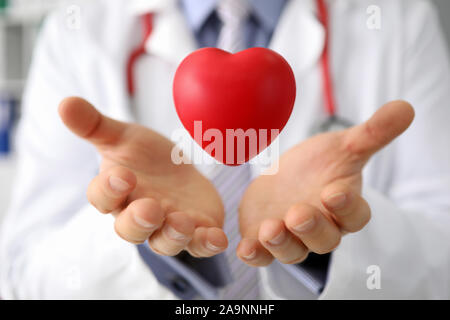 Doctor hold in hand red toy hert against hospital Stock Photo