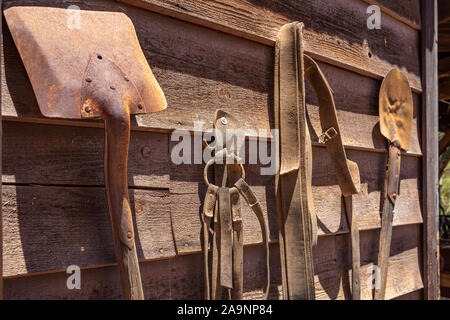 Rusty shovels and worn out leather belts hanging on a wooden wall, sunny spring day in Calico ghost town, California Stock Photo