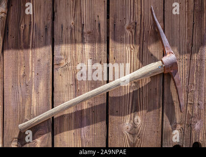 Rusty pick mattock hanging on a wooden wall, sunny spring day in Calico ghost town, California Stock Photo