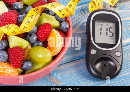 Fresh fruit salad, glucose meter with result of measurement sugar level and tape measure, concept of diabetes, diet, slimming, healthy lifestyles and Stock Photo