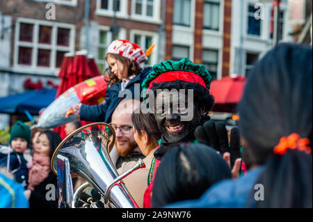 A black-faced helper greeting some children during the event.Like each year the first Saturday after November 11th, the red-and-white-clad Sinterklaas (St. Nicholas) arrives with great fanfare to several Dutch cities. In Nijmegen, the white-bearded legend makes his entrance into the city by sailing down the Waal River and following a route through the city. Along the route around 50 Anti-Zwarte Piet activists 'Kick Out Zwarte Piet' (KOZP) organized a protest against Sinterklaas' black-faced helpers. Also some people Pro Zwarte Piet showed up, the tension was palpable between the two sides. Stock Photo