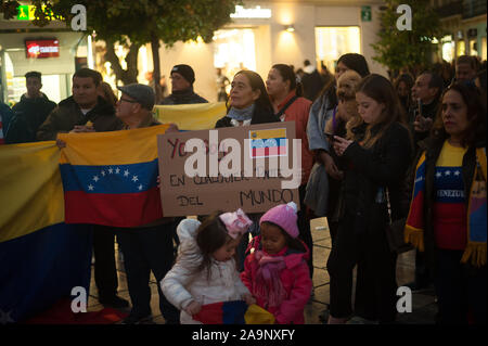 Malaga, Spain. 16th Nov, 2019. Kids next to a woman holding a placard as she sings the national anthem during the protest against Nicolás Maduro government and in support of politician Juan Guaidó, leader of the opposition party and self-proclaimed interim president of Venezuela.A protester is seen holding a Venezuelan flag during the protest against Nicolás Maduro government and in support of politician Juan Guaidó, leader of the opposition party and self-proclaimed interim president of Venezuela. Credit: SOPA Images Limited/Alamy Live News Stock Photo