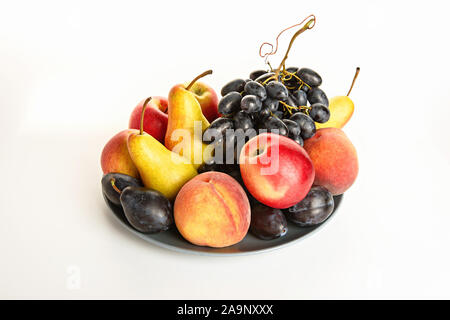Still life with bananas, pears, plums, grapes, apples and peaches on a plate. Stock Photo