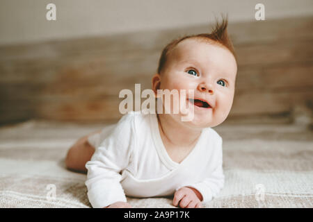 Happy infant baby crawling on bed smiling adorable child ginger hair family lifestyle 3 month old kid positive emotions Stock Photo