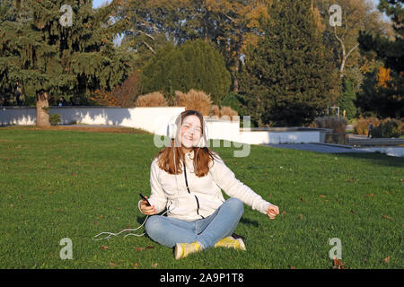happy teenage girl listens to music from her smartphone and sings in park Stock Photo