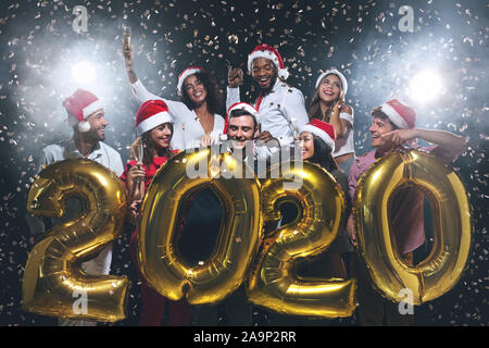 Happy friends greeting New Year 2020, holding golden balloons Stock Photo
