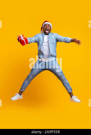Overjoyed afro guy in santa hat jumping with gift box Stock Photo