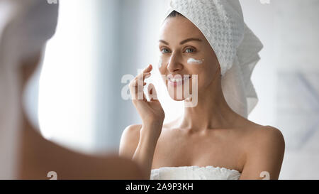 Smiling pretty lady put moisturizing facial cream look in mirror Stock Photo