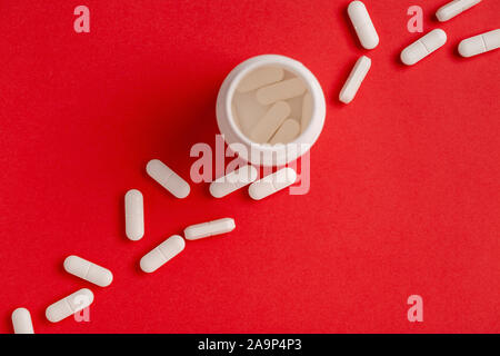 White pills on a red background. plastic white medicine bottle. Top view Stock Photo