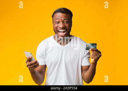 Happy Man Holding Smartphone And Credit Card Standing, Studio Shot Stock Photo