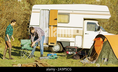 Beautiful young couple getting out of their retro camper van in the wildness. Camping tent. Relaxing weekend. Stock Photo