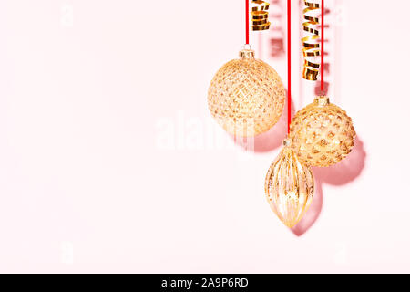 Three golden Christmas baubles hanging against the pink background. Minimal styled New Year concept. Stock Photo