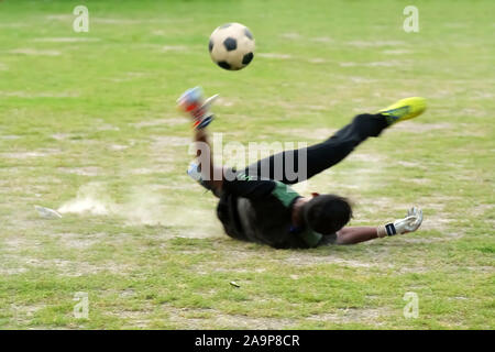 Fit goal keeper is jumping up on green grass filed to save a goal Stock Photo