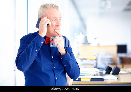 Senior businessman looking thoughfully while sitting in the office and making a phone call. Stock Photo