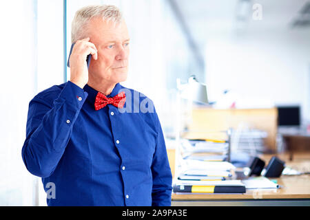 Portrait shot of senior businessman looking thoughtfully while talking with somebody on mobile phone in the office. Stock Photo