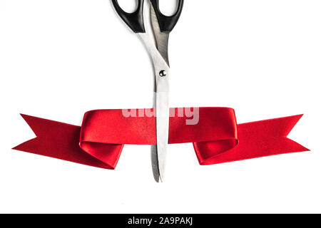Scissors cutting through red ribbon or tape, isolated on white background Stock Photo
