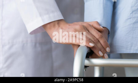 Female doctor holding senior patient hand using walking frame, closeup Stock Photo