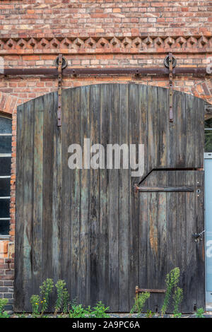 View of a old wooden industrial sliding door on a red brick facade of a building. Vintage Strap Door. Industrial wheel steel barn wood door. Stock Photo