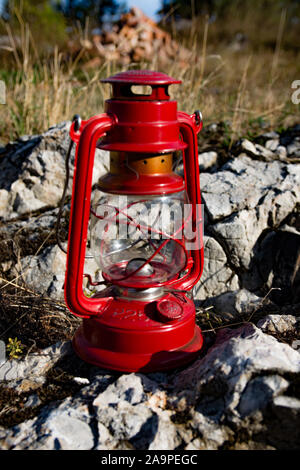 Old red kerosene lamp, standing on a rocks, on meadow, with dried grass in the background. Lamp redy for use. Stock Photo