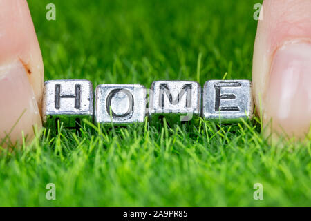 Close up on word HOME written in metal letters laid on grass and held between the fingers of a woman. Concept of ecological house, house in the countr Stock Photo