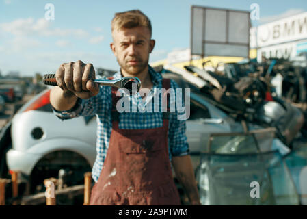 Male repairman shows wrench on car scrapyard Stock Photo