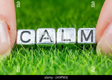 Close up on word CALM written in metal letters laid on grass and held between the fingers of a woman. Concept of wellness, psychology background Stock Photo