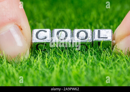 Close up on word COOL written in metal letters laid on grass and held between the fingers of a woman. Concept of wellness background Stock Photo