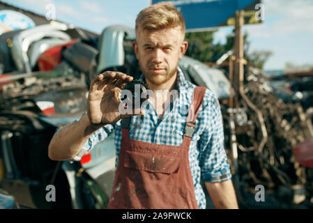 Male mechanic shows gear car on junkyard Stock Photo