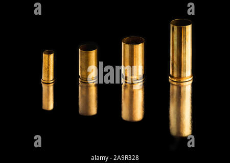 Comparison of sizes of different used bullet shells on a black isolated background with reflection from a tin table top. View of the different caliber Stock Photo