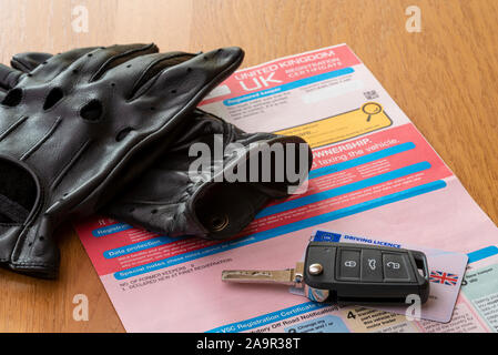 Car key, gloves and V5C document or log book, on a wooden table. Stock Photo