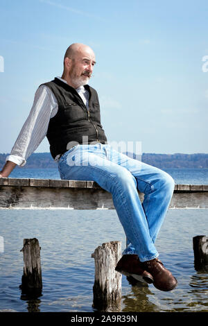 An old man with a grey beard sitting on a jetty Stock Photo
