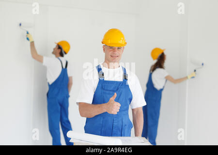 Manual worker gives thumbs up in front of two house painters painting walls Stock Photo