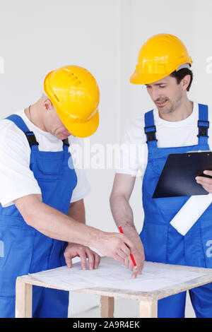 Building, construction, development, teamwork and people concept - close up of builders in hardhats working with blueprint Stock Photo