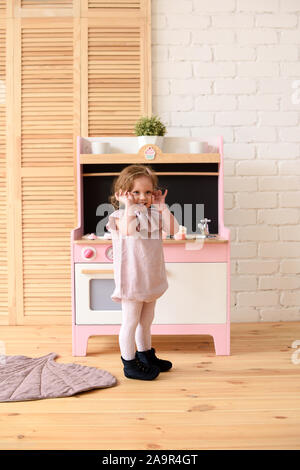Little kid concept. Adorable smiling toddler girl at play kitchen in light room copy space Little kid concept. Adorable smiling toddler girl at play kitchen in light room copy space