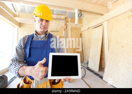 Construction worker holding digital tablet standing at construction site and showing thumb up Stock Photo