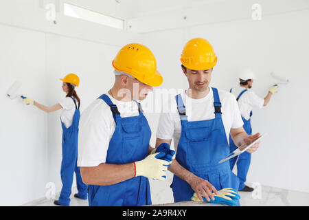 Building, construction, development, teamwork and people concept - close up of builders in hardhats working with blueprint Stock Photo