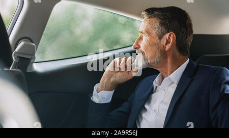 Side view of mature businessman sitting on a backseat of a car and looking out of window Stock Photo