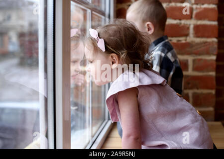 Children or siblings concept. Little girl and boy sitting at window and watching outside close up Stock Photo