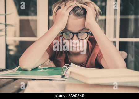 Tired student doing homework at home sitting outdoor with school books and newspaper. Boy weary due to heavy study. Kid asleep on the copybook after l Stock Photo