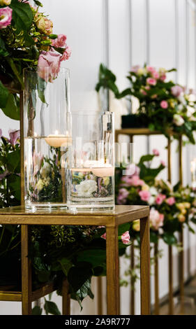 vases with burning candles on the table against the background of flowers, copy space Stock Photo
