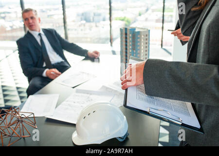 Meeting of architects and business investors, model of modern multi storey residential building house plans and hardhat on table , construction planni Stock Photo
