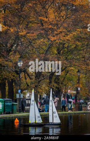 London, UK. 17th Nov 2019. Remote control yachts make slow progress in the light breeze - Autumn trees reflect in the boating lake on Clapham Common, London. Credit: Guy Bell/Alamy Live News