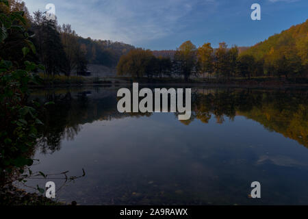 Fresh water lake in a former quarry with reflections of the Indian summer and autumn colors of the leaves on an early morning in November Stock Photo