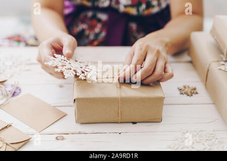 Close up of hands holding wrapping gift box on wooden table with xmas decoration. Stock Photo