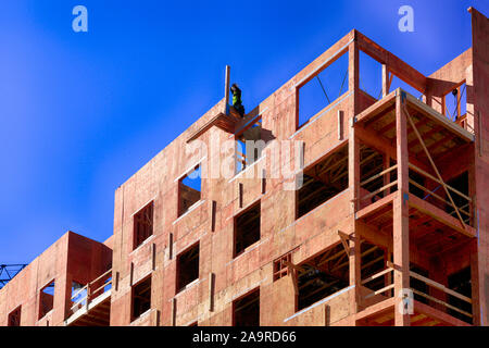 Man perched high up on a wooden inner skeleton of a new apartment building in downtown Tucson AZ Stock Photo