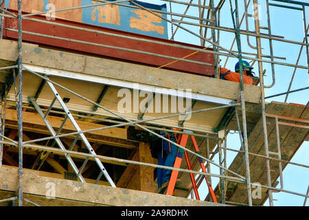 Two construction workers wearing safety equipment go about their jobs high up on scaffolding at an apartment building project in Tucson AZ Stock Photo