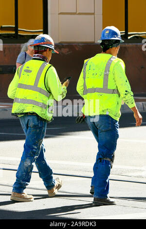 Two construction workers wearing their hard-hats and high viz vests walk back to their jobs on a downtown project in Tucson AZ Stock Photo