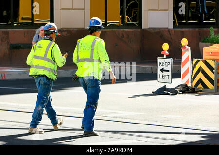 Two construction workers wearing their hard-hats and high viz vests walk back to their jobs on a downtown project in Tucson AZ Stock Photo